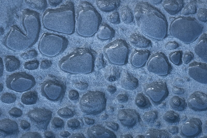 Close-up view of water droplets scattered on a smooth blue surface, with droplets varying in size and shape, creating a textured and reflective appearance.