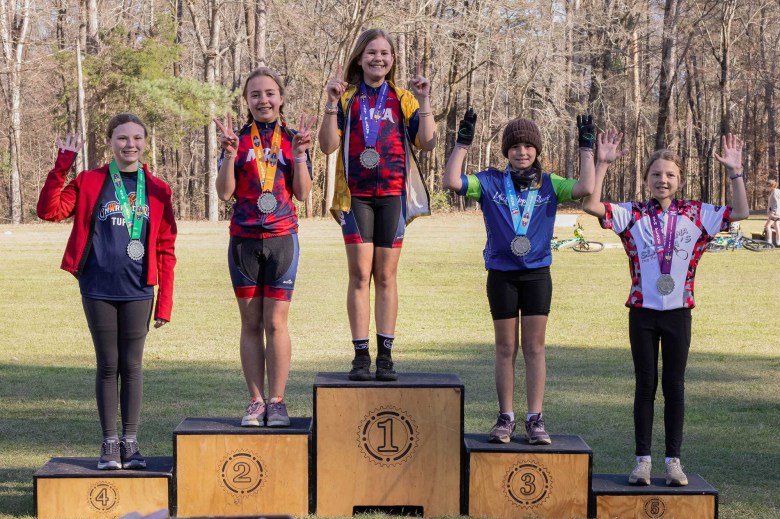 Five girls stand on an outside awards podium, medals around their necks