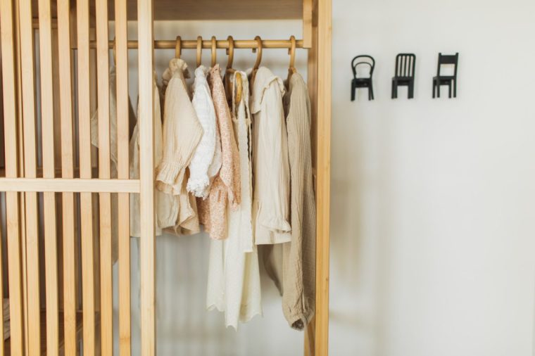 Children??????s clothes hanging on rail in wooden closet at home. Fashion and shopping concept. Modern closet interior design concept.
