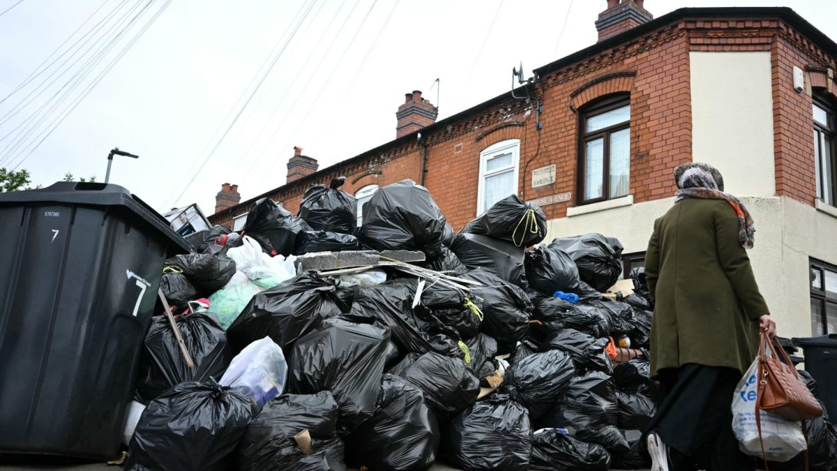 A resident walks past uncollected bin bags piled up on Poplar Road in Birmingham, central England, on April 15, 2025. Residents are desperately trying to get rid of an estimated 17,000 tonnes of trash that has piled up since refuse workers ramped up a strike last month. Four weeks in, the city council has declared a "major incident," the prime minister has had to defend the government's response in parliament, and residents say their problems are worsening by the day. (Photo by Paul ELLIS / AFP) (Photo by PAUL ELLIS/AFP via Getty Images)