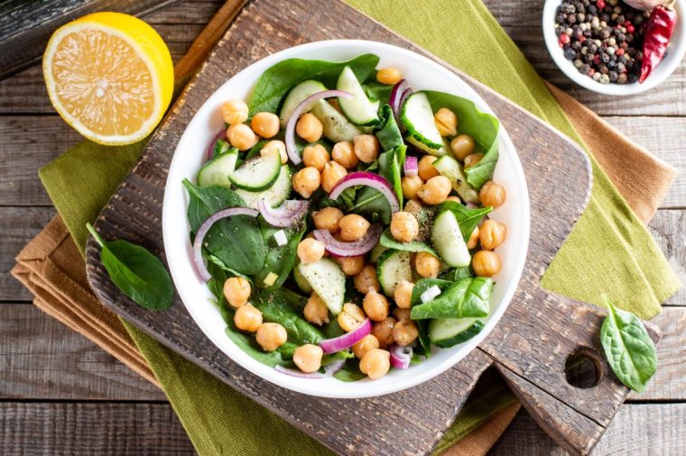 Green vegetable salad with chickpea, spinach, cucumber, red onions, and greens on a wooden table. Top view