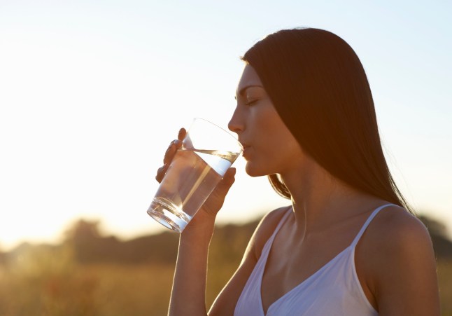 A woman outside in the sun, drinking a glass of water