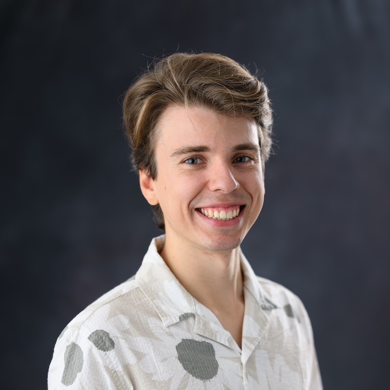 Smiling man with wavy hair wearing a shirt with flower shapes on it.