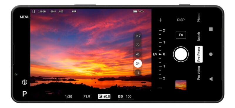 A smartphone screen shows a camera app interface capturing a vivid sunset over water with islands and clouds, featuring camera settings and controls displayed on the right side.