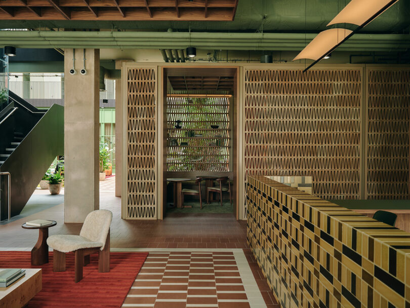Modern interior with earthy tones featuring a checkered tile floor, wooden furniture, a textured wall, and a partially visible staircase. A table with chairs sits in a recessed alcove.