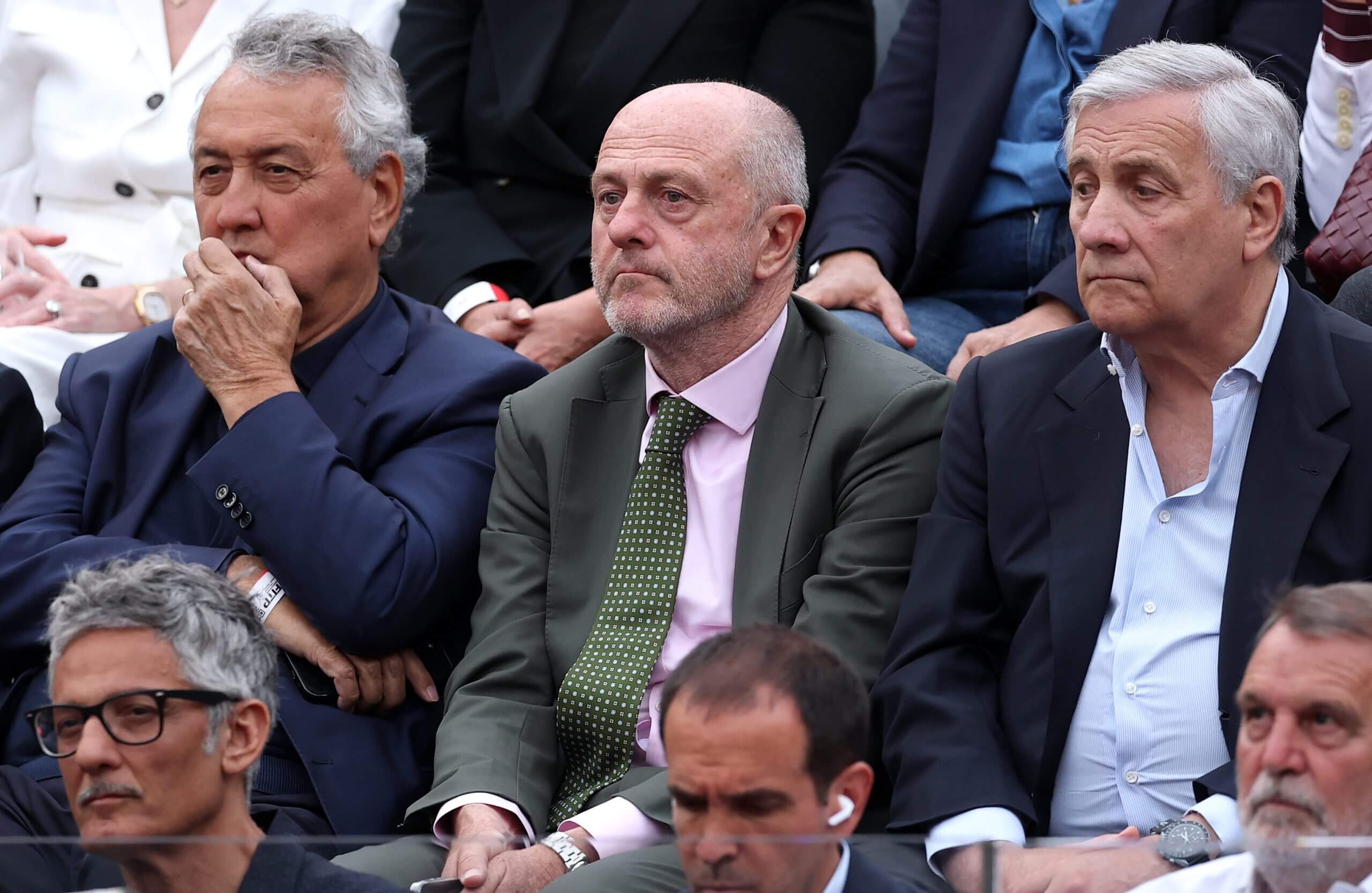 Angelo Binaghi (center) sits in a suit with a green tie between two more men in suits in a sports crowd.