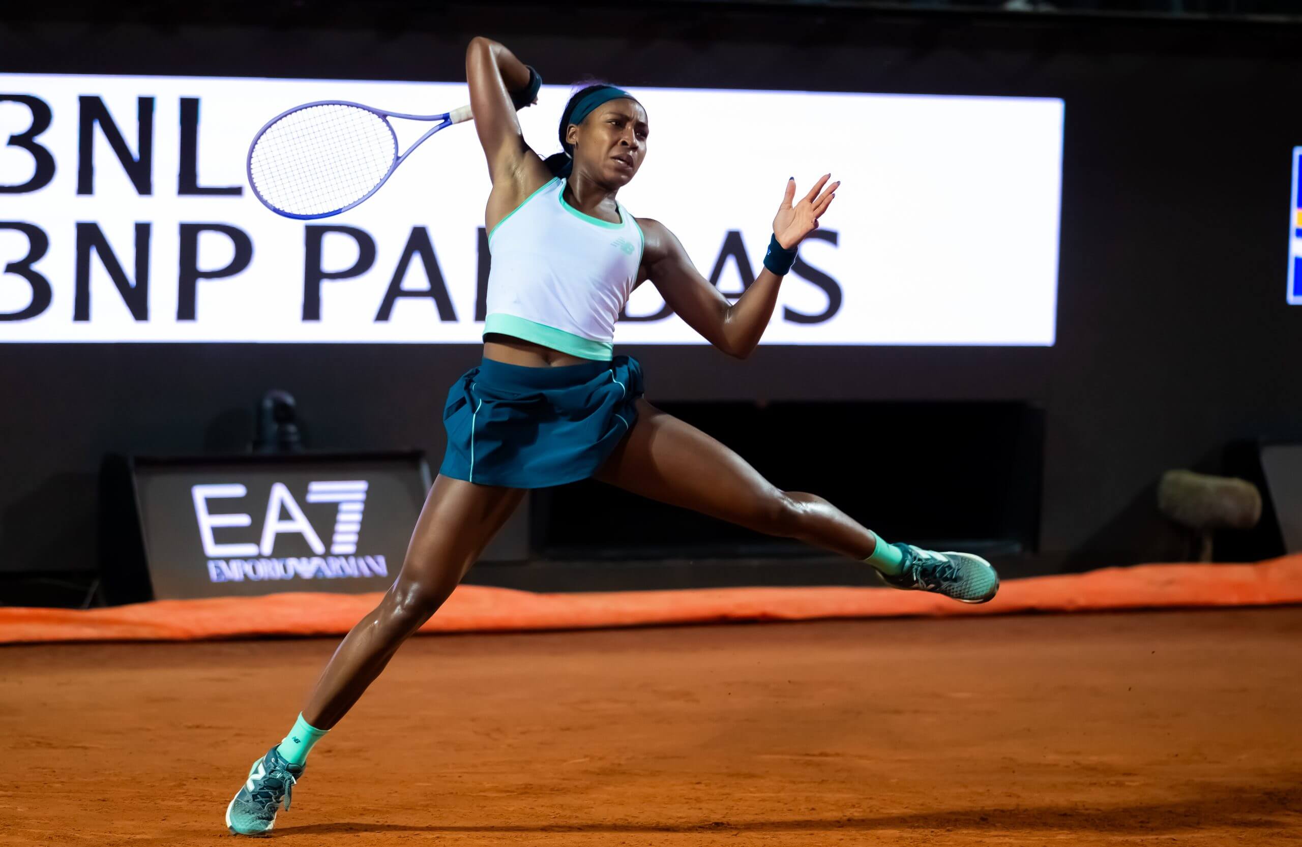 Coco Gauff follows through on a forehand while balanced on the toe of her right foot, on a clay tennis court.