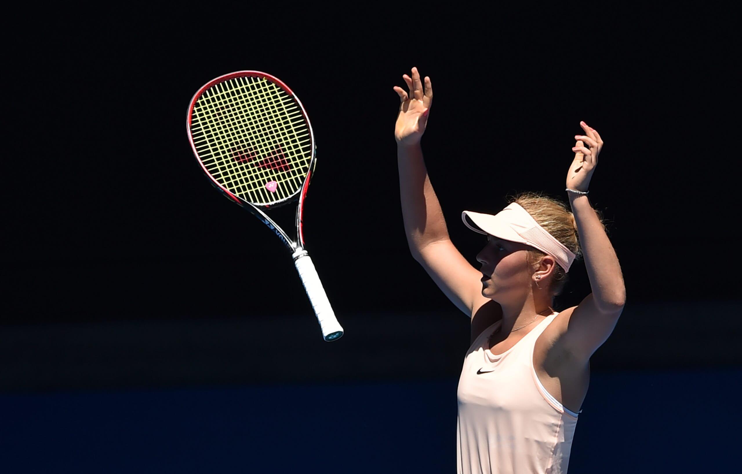 Marta Kostyuk throws her hands and racket in the air in celebration.