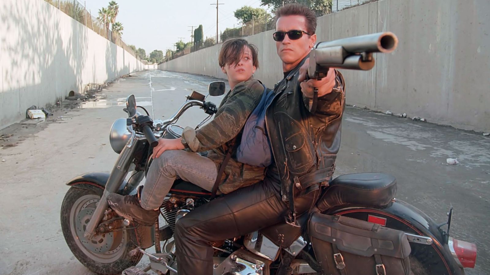 Image may contain Arnold Schwarzenegger Edward Furlong Clothing Coat Jacket Adult Person Glove Gun and Weapon