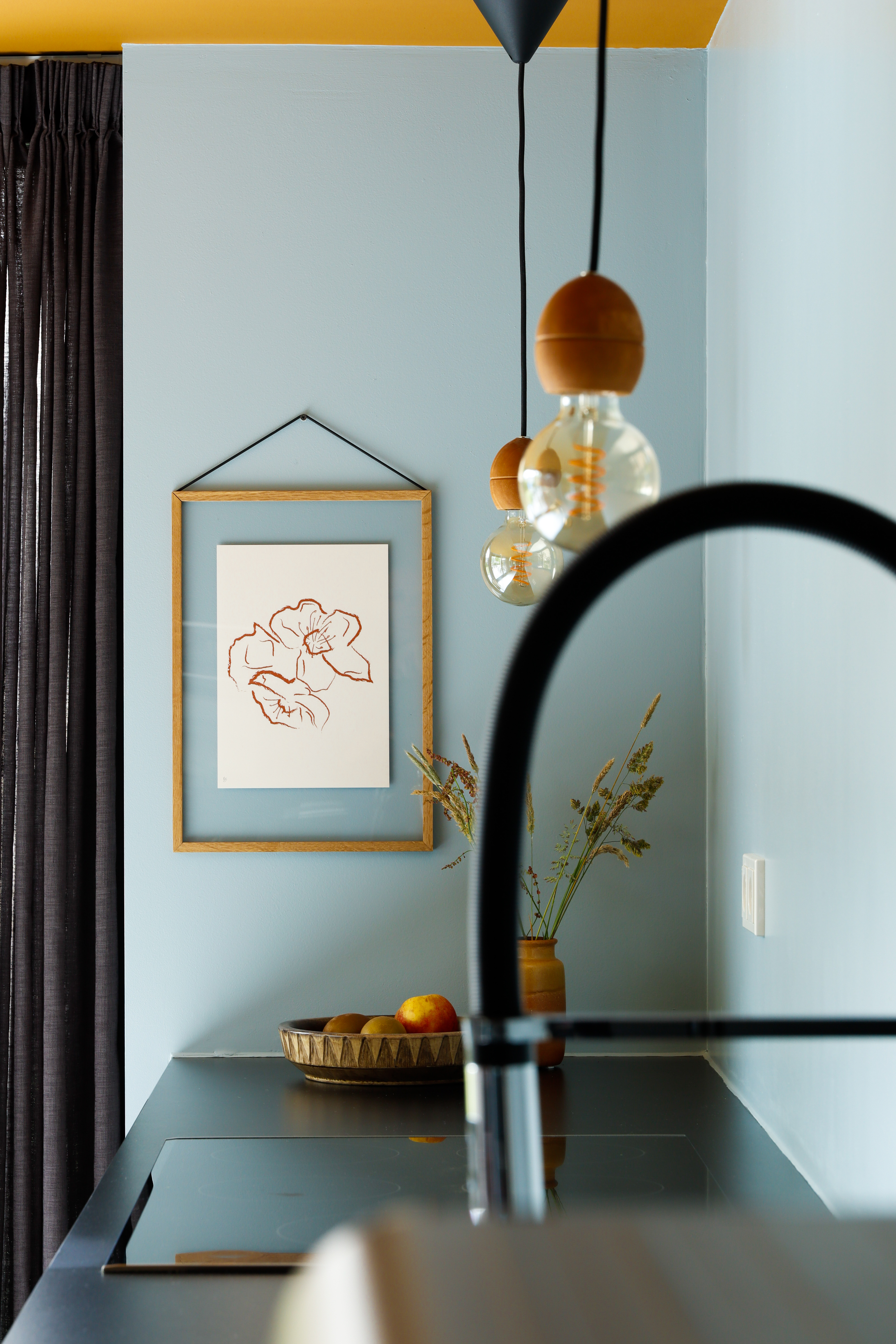 A mineral blue wall in a kitchen with framed artwork and a yellow painted ceiling