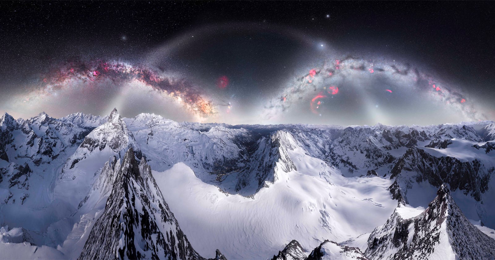 Snow-covered mountain peaks under a dark sky with bright, colorful arcs resembling galaxies and nebulae, creating a surreal and otherworldly landscape.