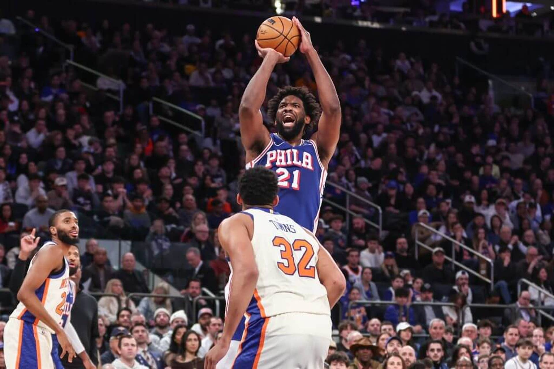 Joel Embiid raises up to shoot the ball. Karl-Anthony Towns faces him in defense.