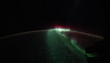 The curve of the Earth against space is highlighted by a bright green streak of light down the middle with some pink light near the top.