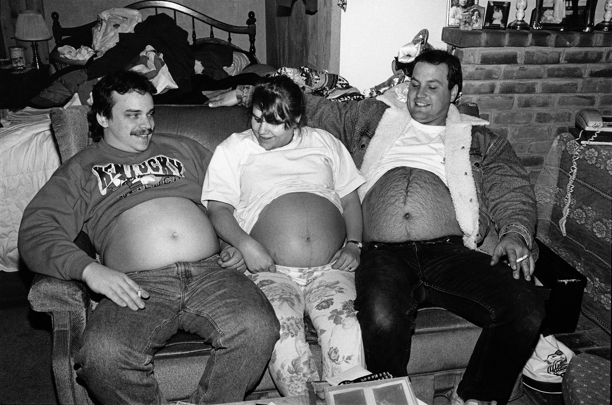 Adults sat on sofa with their tops pulled up revealing their bellies.