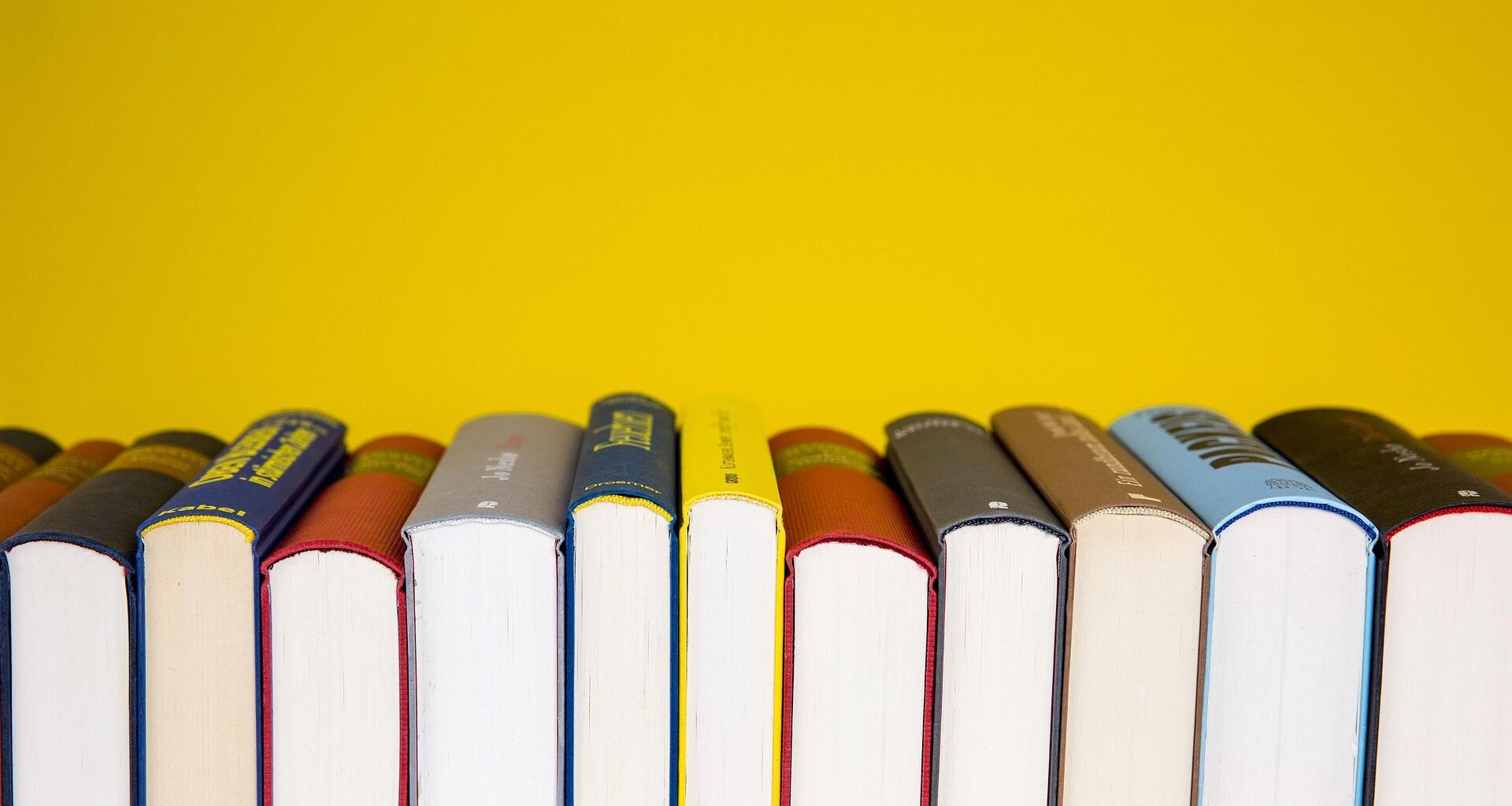 A series of books stacked horizontally so we only see the bottom of their pages with a bright yellow background behind.
