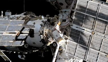 Two spacesuited cosmonauts are seen working outside a large space station set against the blackness of space.