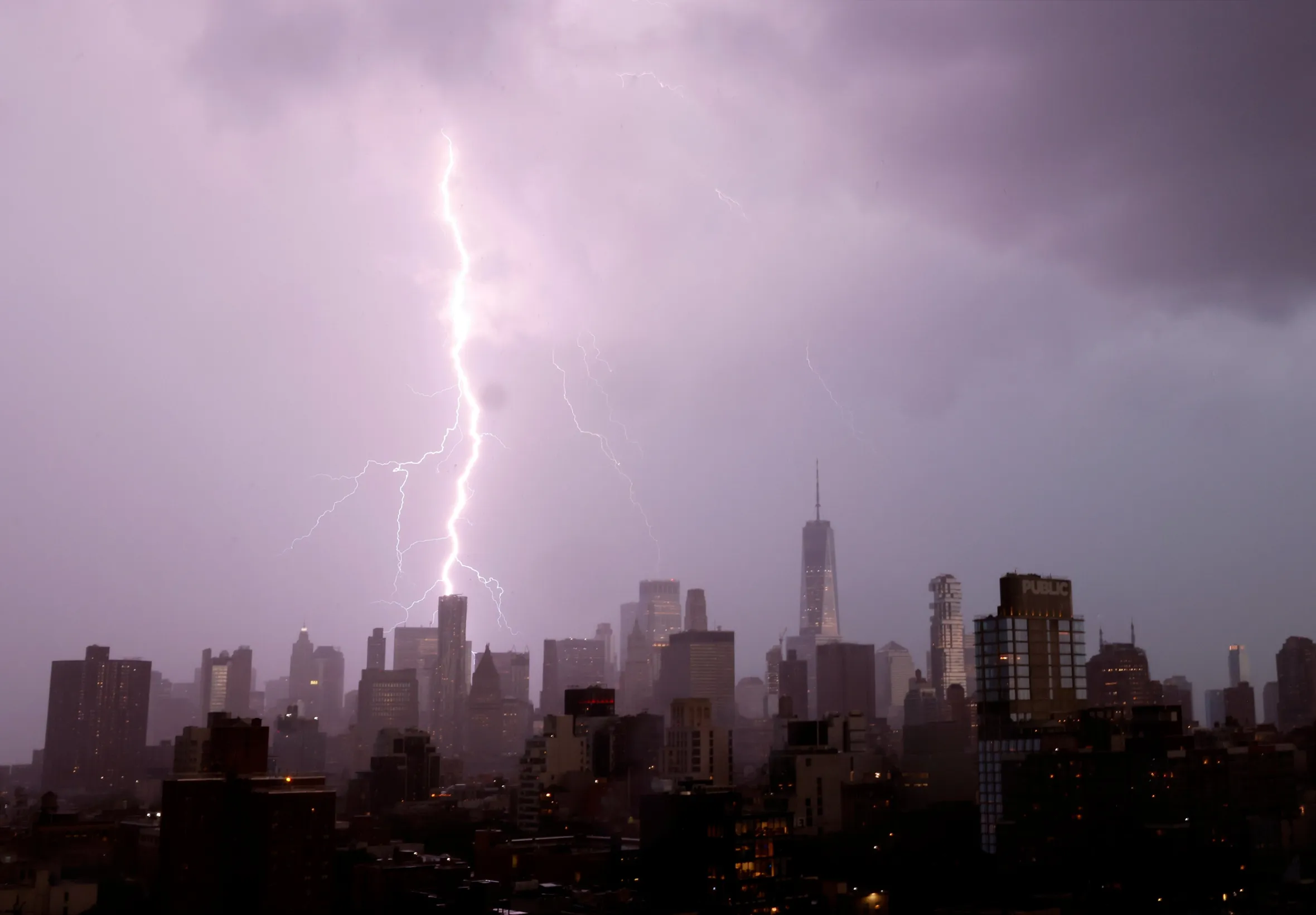 Lightning strikes a building in the Manhattan skyline under dark storm clouds.