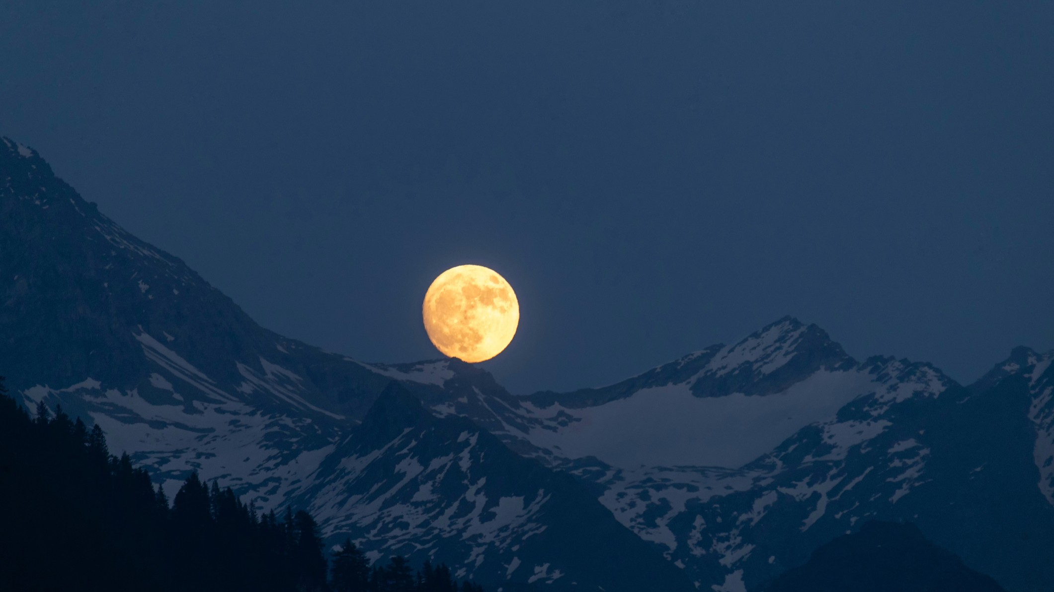 bright full moon rising above snow-capped mountains.