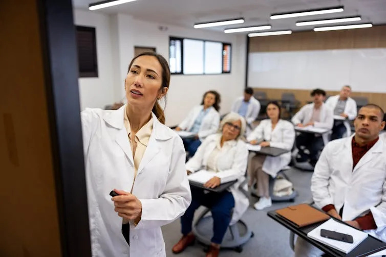 Woman writing on the board while teaching a class to a group of people in white coats