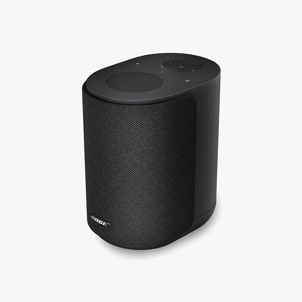 Black Bose smart speaker with fabric grille and touch controls on top against a white background.