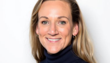 Portrait of a smiling blonde woman with green eyes wearing a navy turtleneck