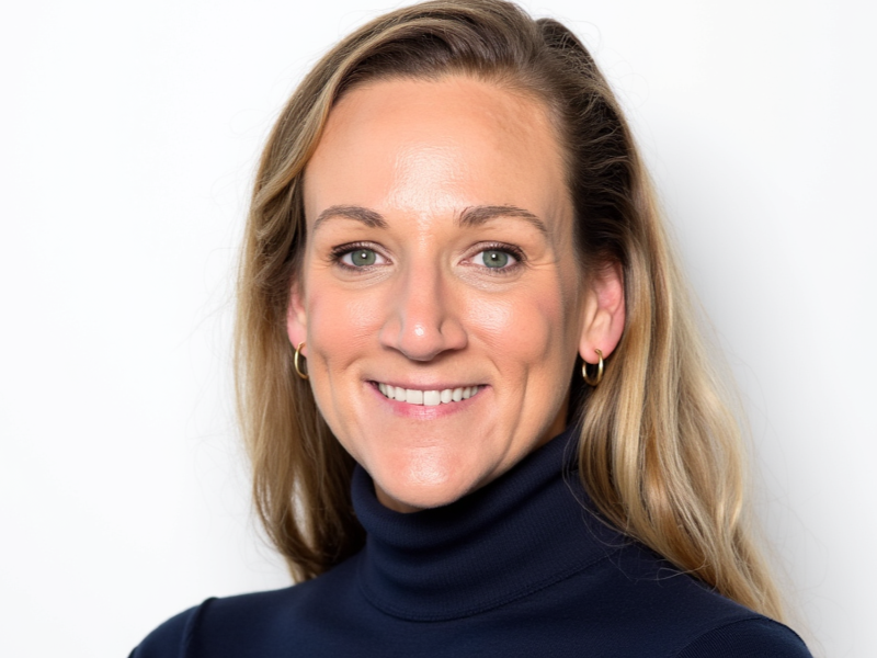 Portrait of a smiling blonde woman with green eyes wearing a navy turtleneck