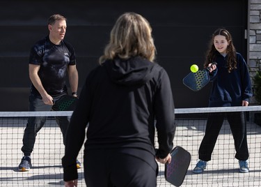 Three people dress in black playing pickleball.