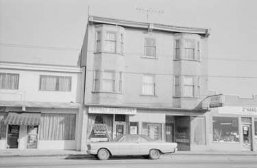 1974: An exterior view of 3934-3938 Main St. The business sign for Bombay Restaurant is visible.