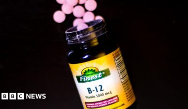 A bottle of vitamin B12 supplements. A handful of round-shaped pink tablets are shown near the rim of the bottle, which has a yellow label.