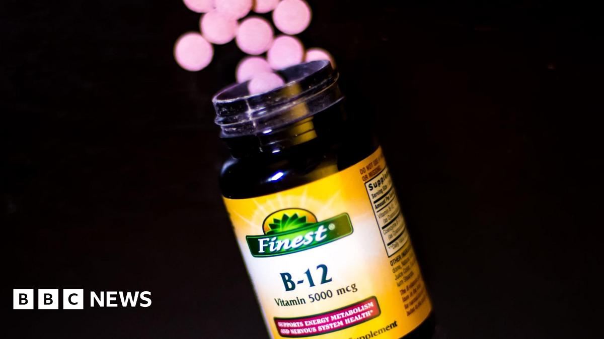 A bottle of vitamin B12 supplements. A handful of round-shaped pink tablets are shown near the rim of the bottle, which has a yellow label.