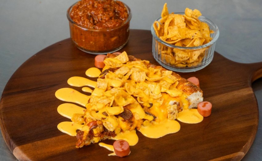 A freshly baked Bow Tie Pizza topped with sliced hot dogs, hearty chili, melted cheese, and a crispy crust.