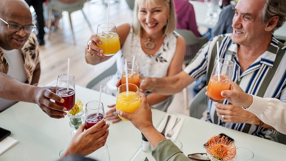 Senior friends toasting with drinks at a restaurant table