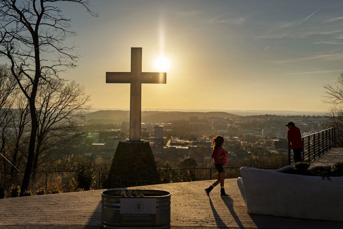 A girl walks past the cross atop Mount Sequoyah, a hilltop landmark and overlook above Fayetteville, Arkansas.