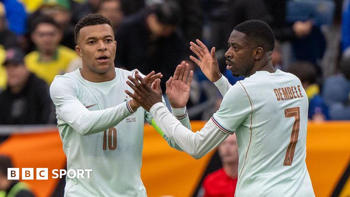 Kylian Mbappe (left) and Ousmane Dembele (right, photographed from behind), both wearing white France shirts, high five one another