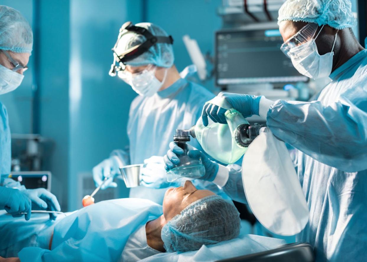 Anesthetist holding oxygen mask above patient. - 