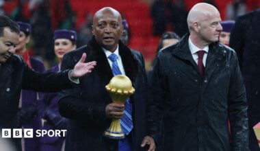 Caf president Patrice Motsepe, centre and dressed in a long black coat and white shirt and blue tie, carries the Africa Cup of Nations trophy in his right hand as he walks flanked by Fifa president Gianni Infantino.