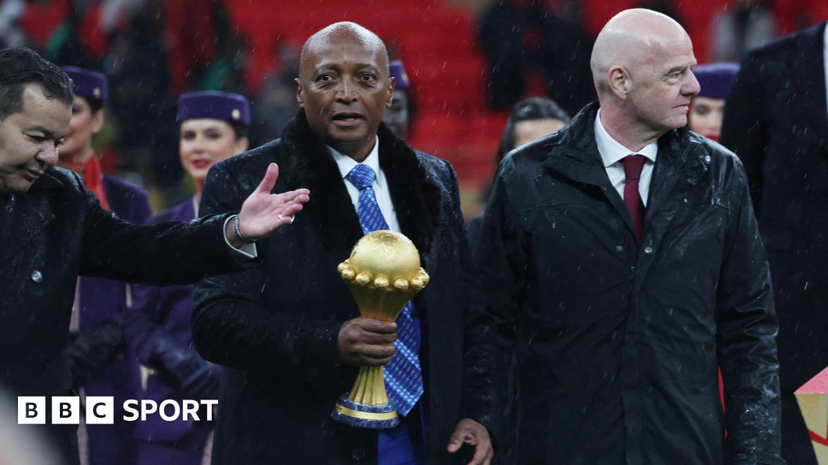 Caf president Patrice Motsepe, centre and dressed in a long black coat and white shirt and blue tie, carries the Africa Cup of Nations trophy in his right hand as he walks flanked by Fifa president Gianni Infantino.