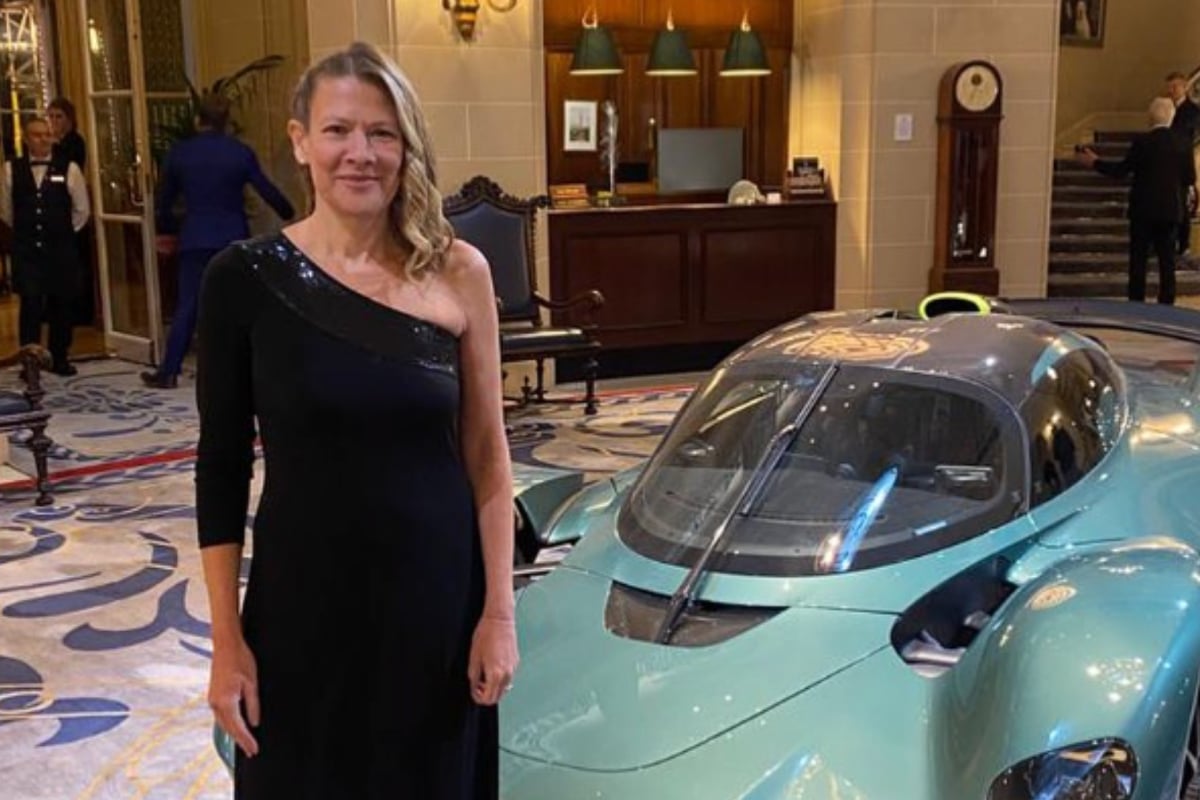 Jennie Gow stands in a black dress in front of turquoise super car