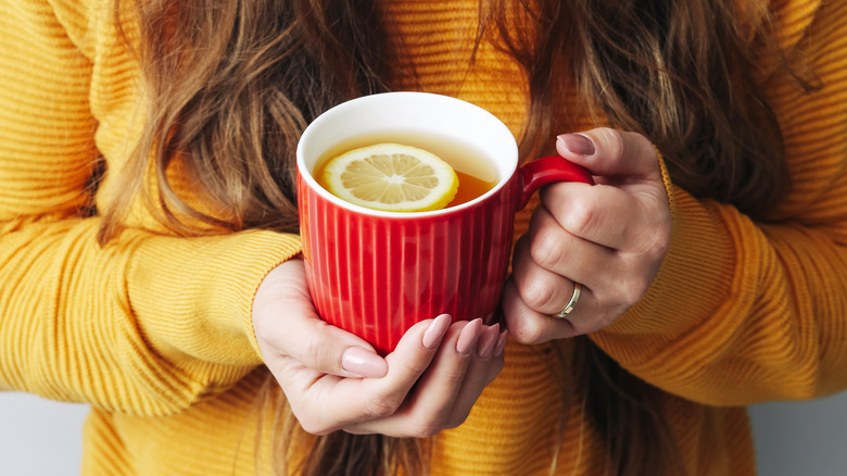 A woman holding a cup of tea with a slice of lemon.