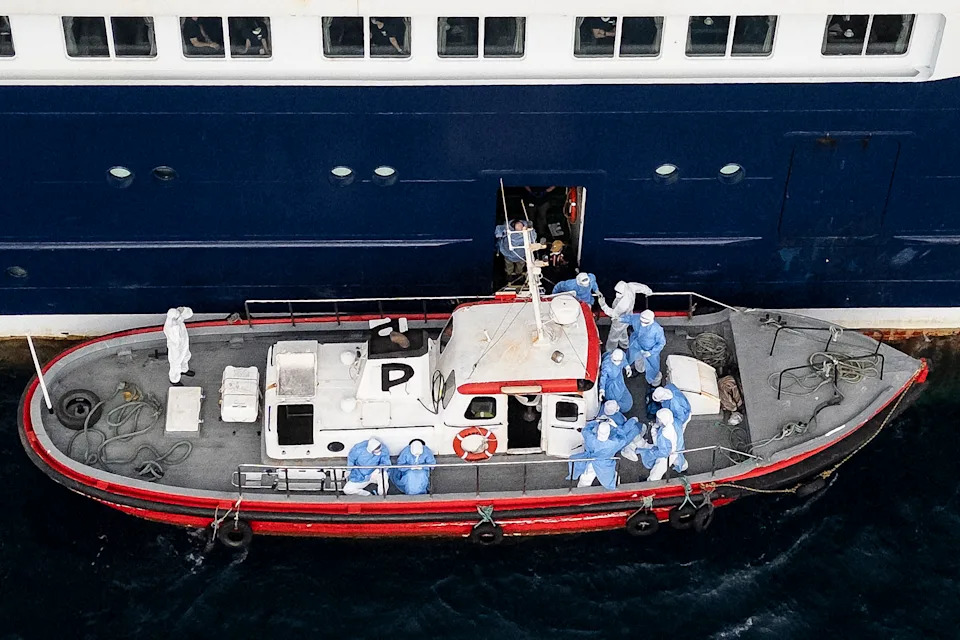 Health personnel helping patients onto a boat from the MV Hondius