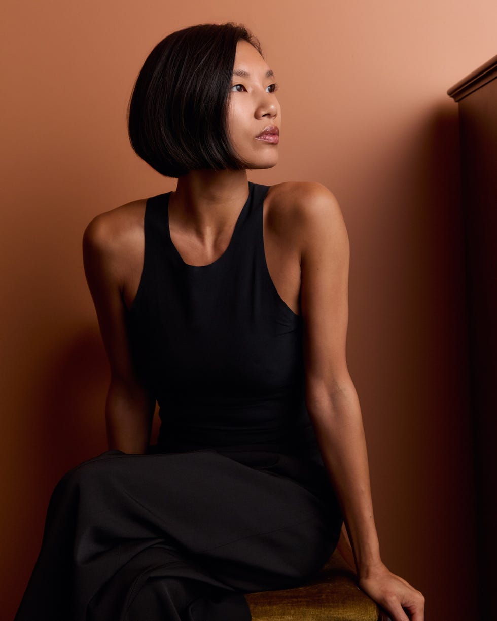 Person sitting against an orange wall, wearing a black outfit.
