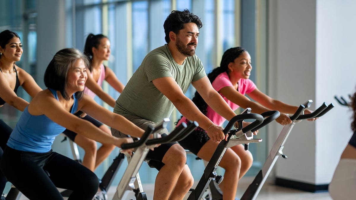 A small group of mature adults sitting on stationary bikes in a fitness class.