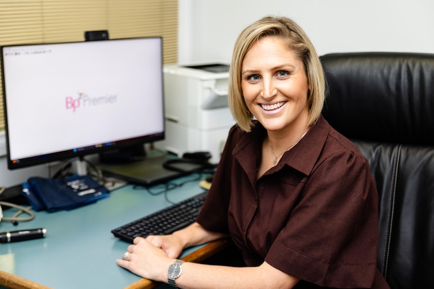 A woman with blonde hair sitting smiling at a desk