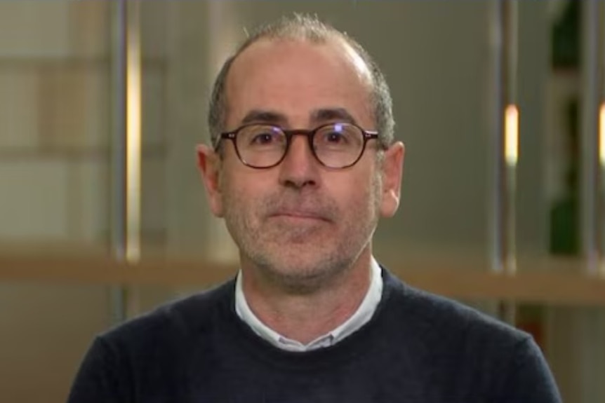 A headshot of a smiling man wearing glasses.