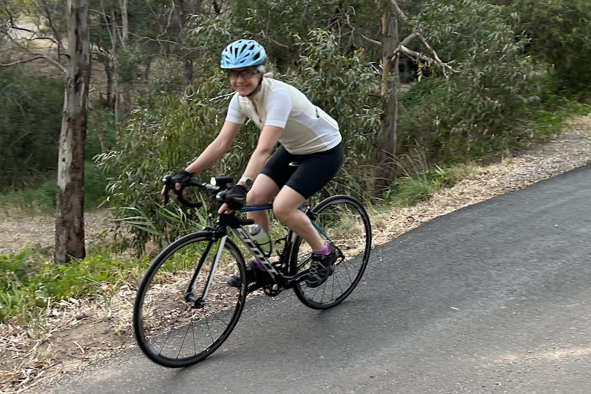 A woman cycling with her helmet down a slope road with trees on the roadside