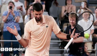 Novak Djokovic, wearing a peach polo shirt, dances with his racquet in his left hand