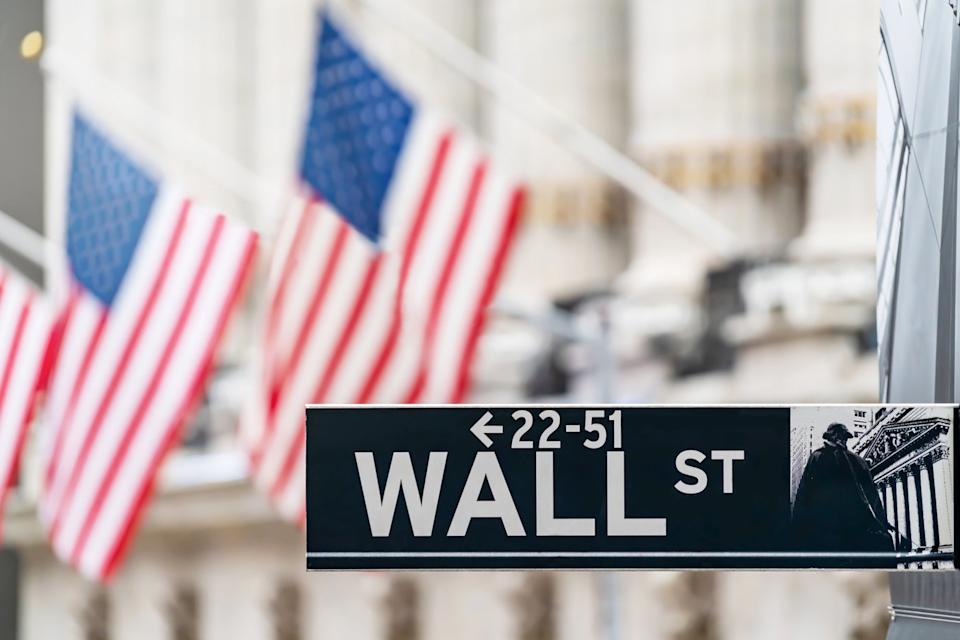 Wall Street sign in front of American flags.