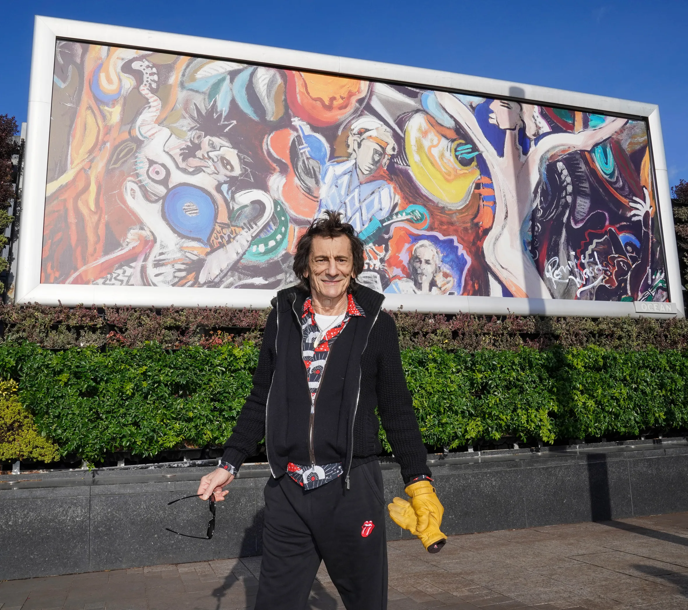 Ronnie Wood in front of a giant billboard of his new painting of The Rolling Stones.