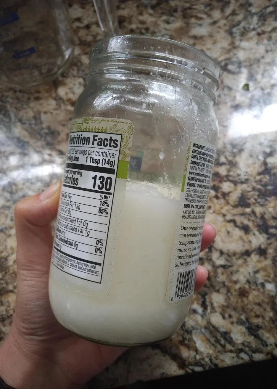 Hand holding a jar of coconut butter with visible nutrition facts label. Jar is placed on a marble countertop