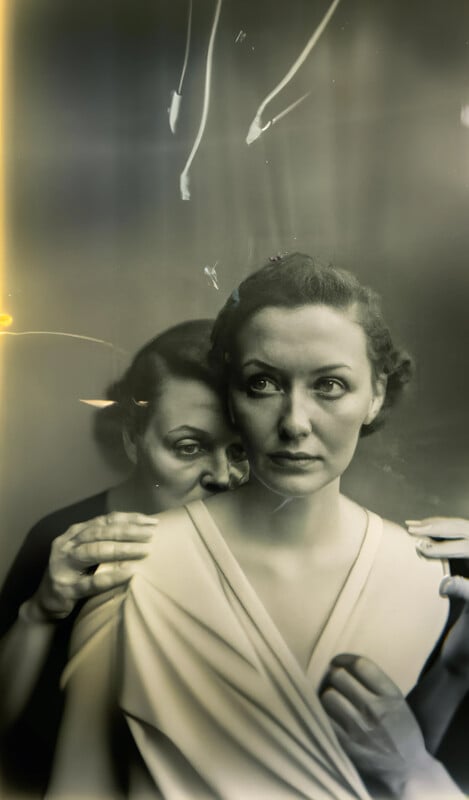 A sepia-toned, surreal image of two women; one stands behind the other, resting her hands on the first woman's shoulders, with ethereal light streaks and scratches adding a haunting, vintage atmosphere.
